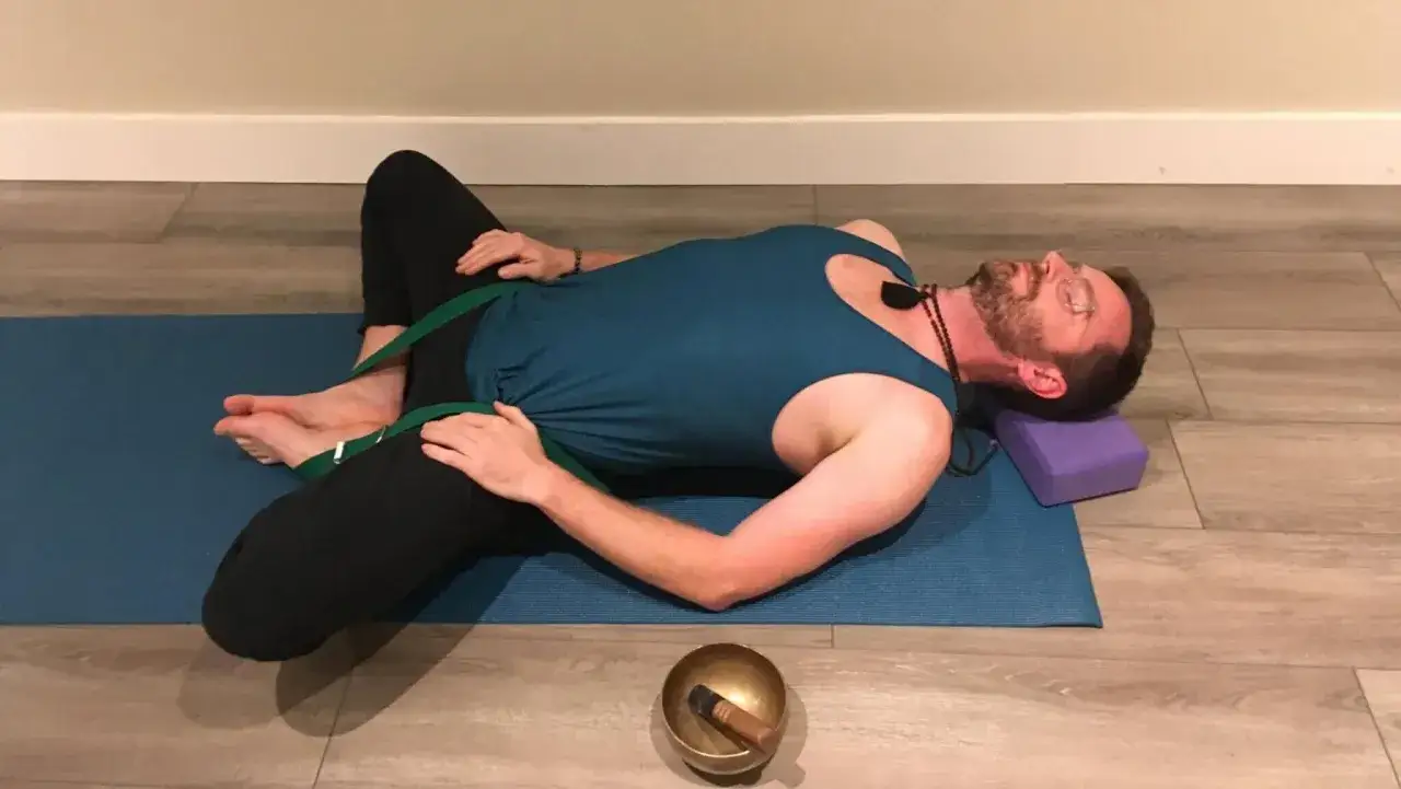 Uomo in posa yoga con cinghia per alleviare i sintomi del secondo chakra bloccato.