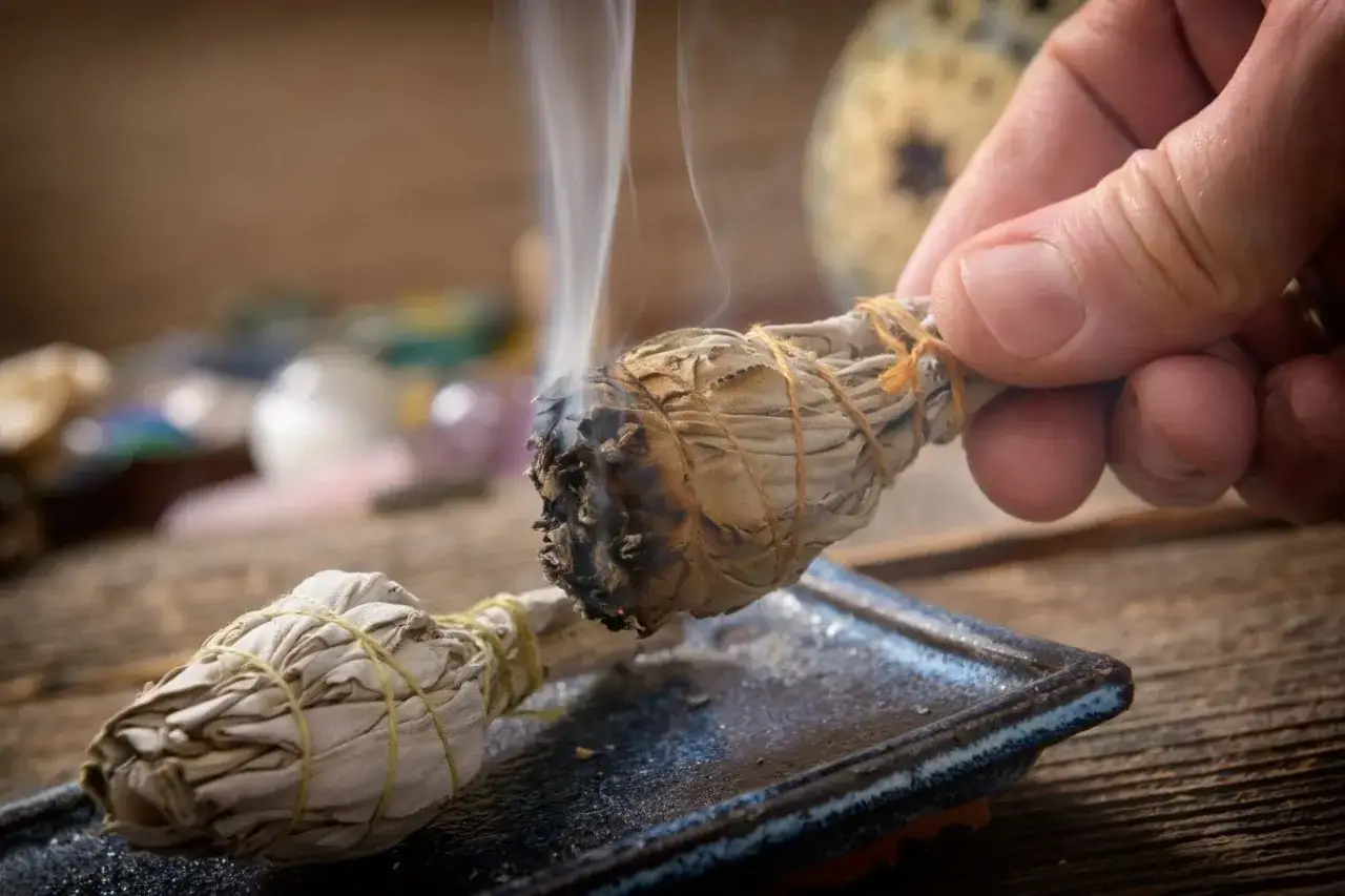 Fumante mazzo di salvia, con cristalli sullo sfondo, per purificare e sfruttare le sue proprietà magiche.