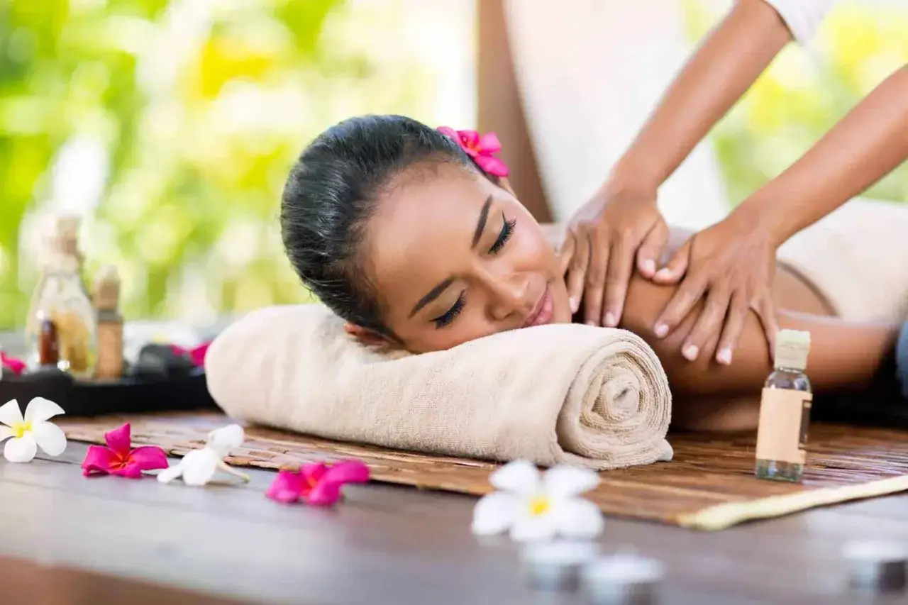 Donna sorridente riceve un massaggio rilassante tutto il corpo, con fiori e oli da massaggio su un lettino da spa all'aperto.