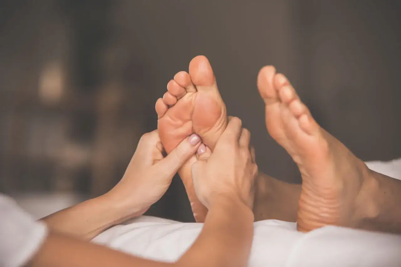 Mani esperte massaggiano un piede, un gesto antico che racconta la storia del massaggio e del benessere.