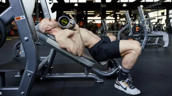 Uomo calvo esegue panca inclinata con bilanciere, uno dei fondamentali esercizi palestra per la parte alta del corpo.