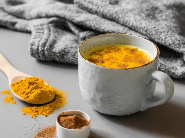 Un latte dorato speziato, perfetto cosa bere al posto del caffè. Curcuma e cannella in una tazza calda, con una coperta grigia sullo sfondo.