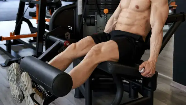 Uomo scolpito esegue un **circuito gambe e glutei** in palestra, concentrato sull'allenamento dei quadricipiti con la macchina.