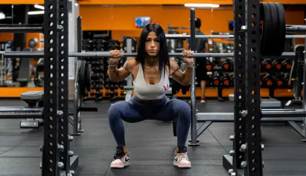 Donna in palestra esegue uno squat con bilanciere, dimostrando come fare bene gli squat con tecnica e concentrazione.