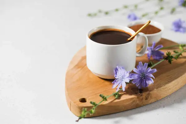 Tazza di caffè di cicoria scuro su tagliere di legno, decorata con fiori di cicoria viola.