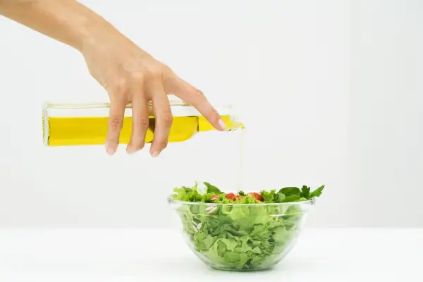 Mano versa olio su un'insalata fresca, un passo per un'insalata per dimagrire gustosa e salutare.