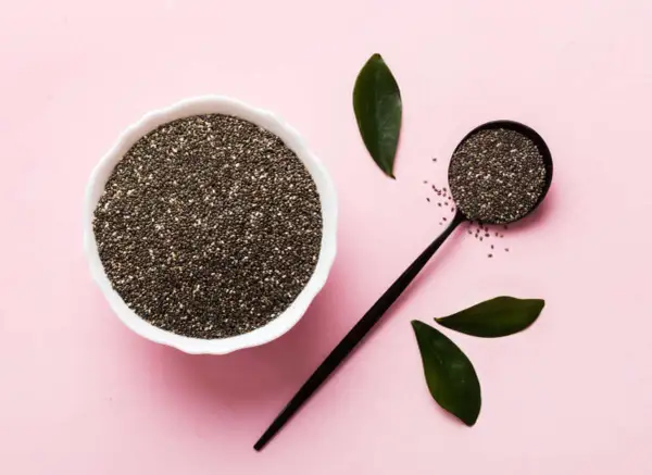 Semi di chia in una ciotola e un cucchiaio, con foglie verdi. Un aiuto naturale per la menopausa.
