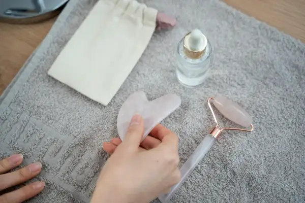 Mano che tiene una pietra gua sha rosa, accanto a un rullo di quarzo e un siero. Utile per il benessere, ma attenzione alle gua sha controindicazioni.