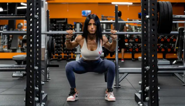 Donna in palestra esegue uno squat con bilanciere, dimostrando come fare bene gli squat con tecnica e concentrazione.